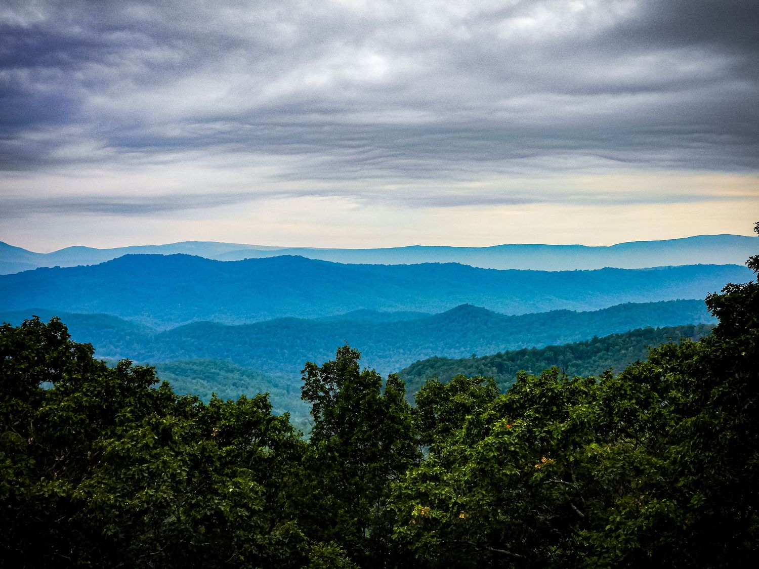 Layered blue mountain ridges fade into the distance under dramatic cloudy skies.