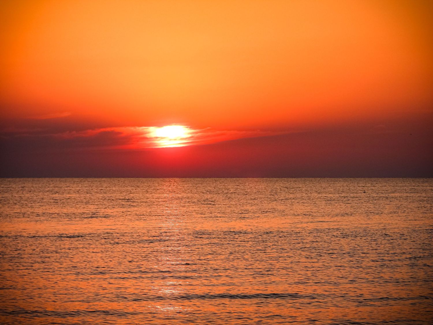 Bright orange sun sets over tranquil ocean creating dramatic colors in the evening sky.