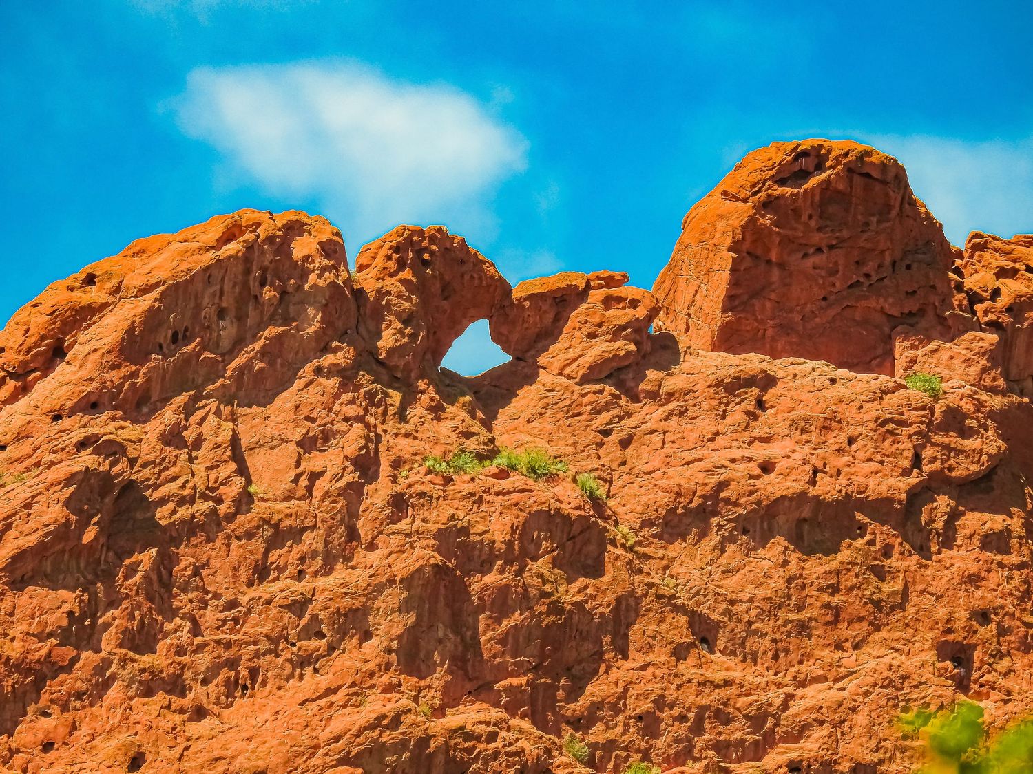 Natural stone arch formation carved into red sandstone cliffs against bright blue sky.