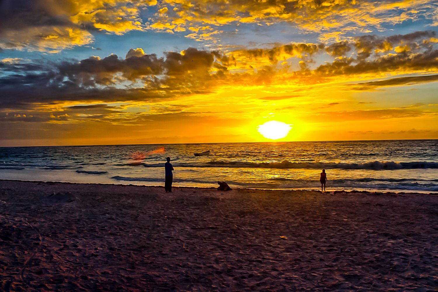 Spectacular golden sunset over beach with silhouettes against orange sky.