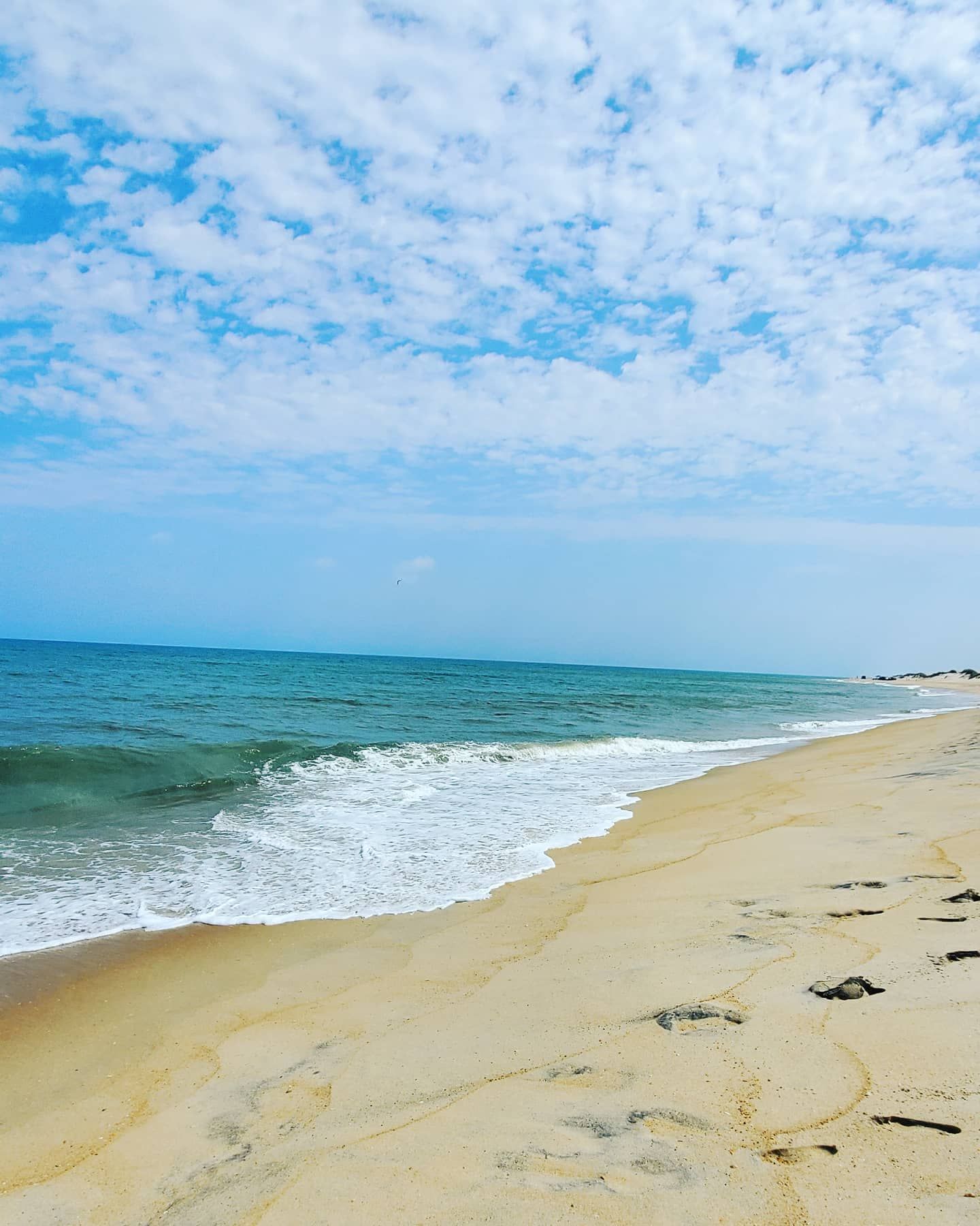 Pristine beach with turquoise waters and white breaking waves under scattered clouds on sunny day.