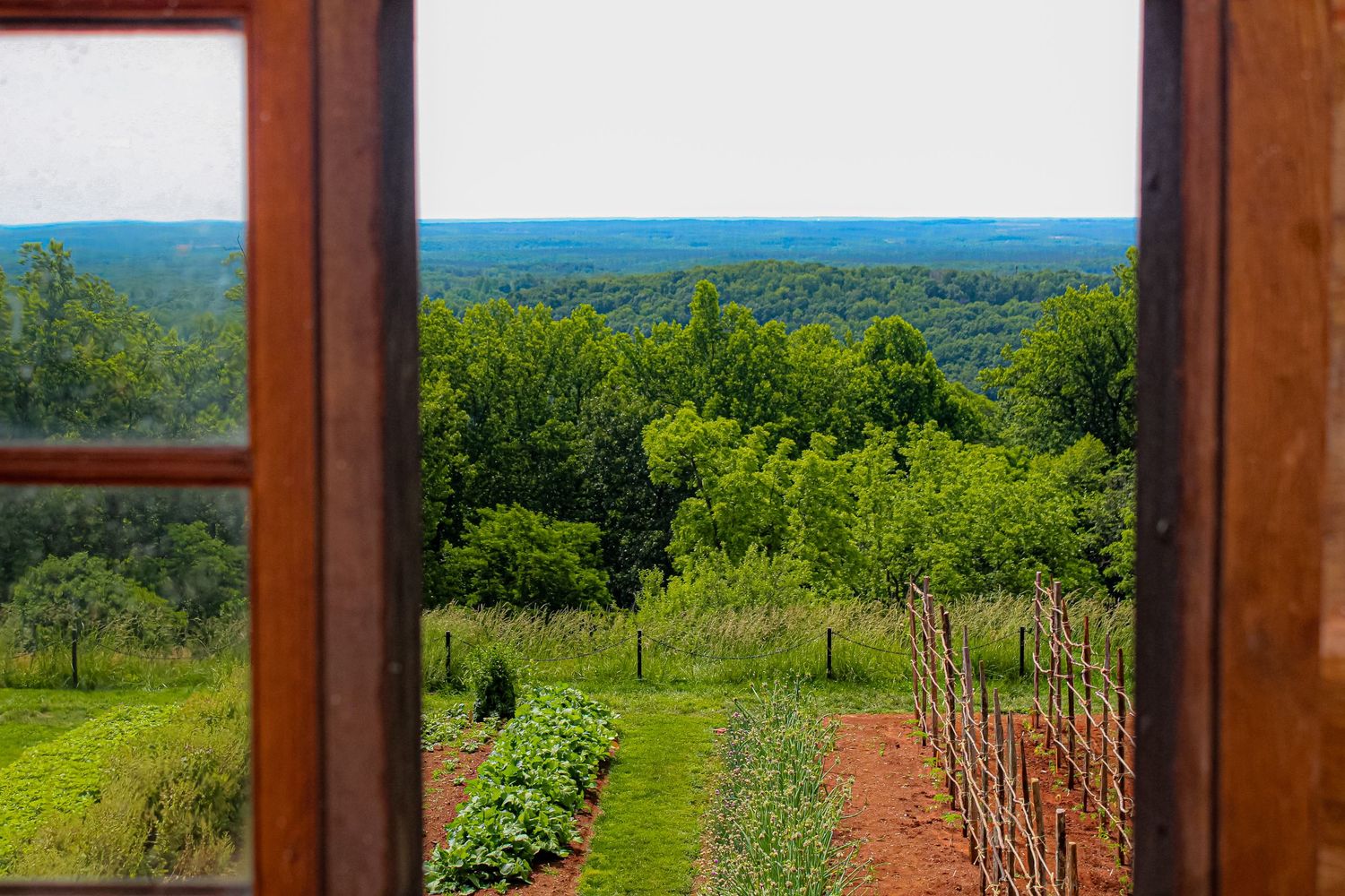 Garden view through window frame overlooking green rolling hills and distant mountains.