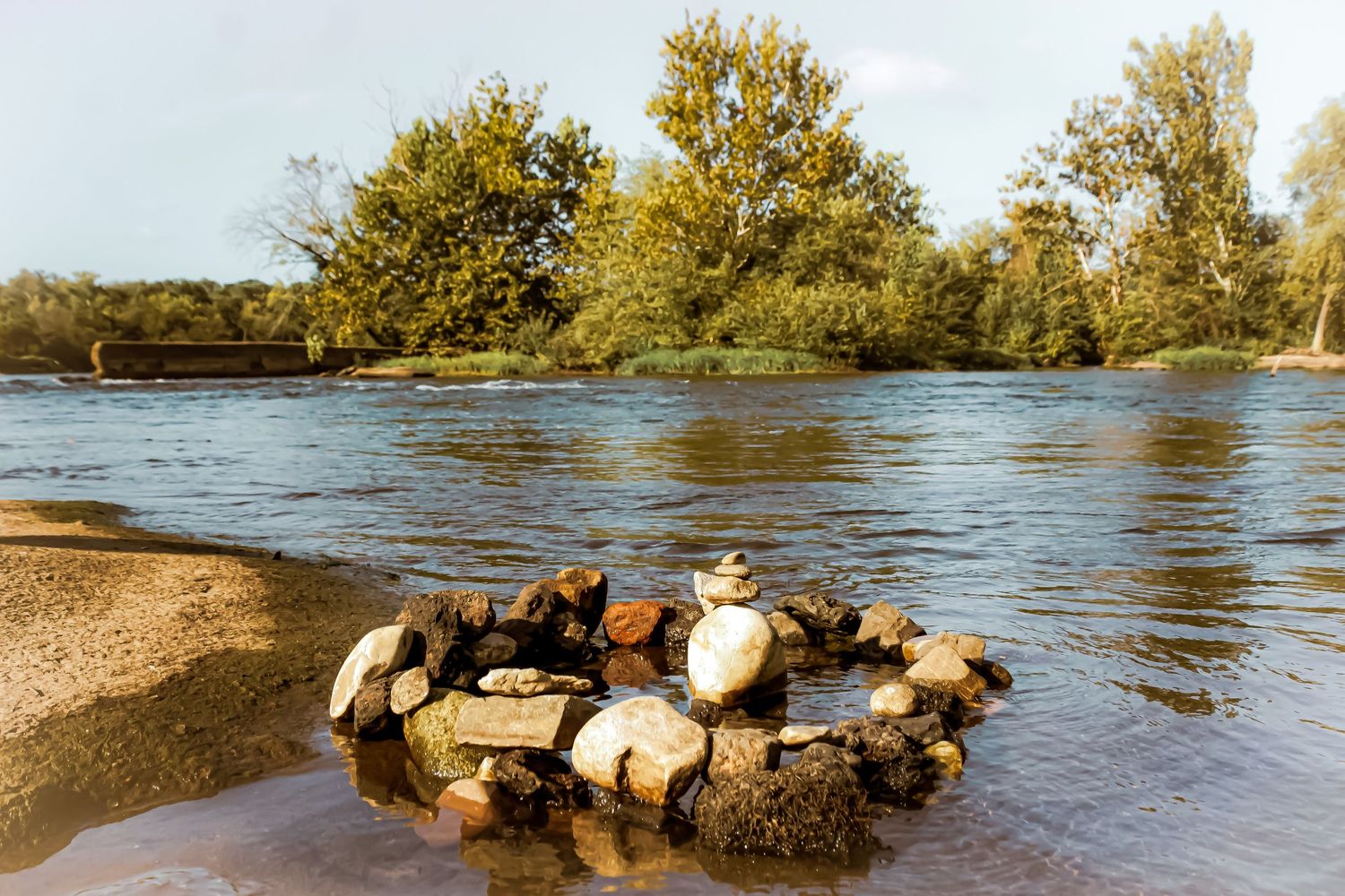 Rock formation in flowing river water with autumn trees in the background.