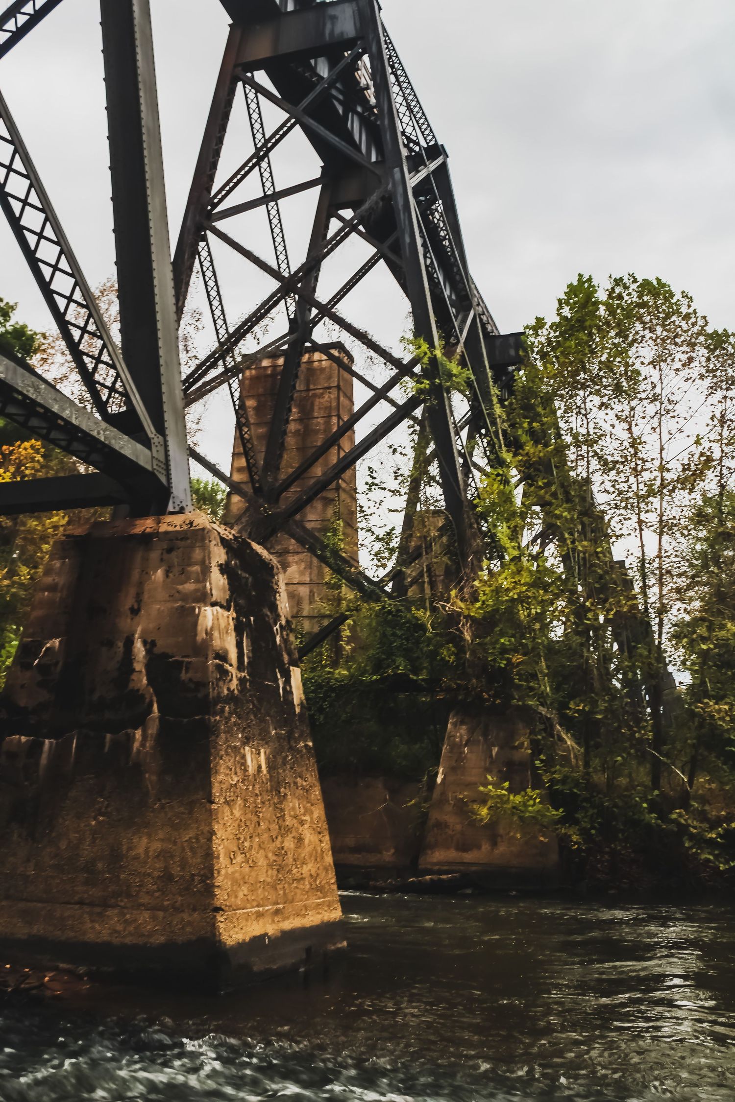 Historic steel railroad bridge with stone supports spanning across a rushing river.
