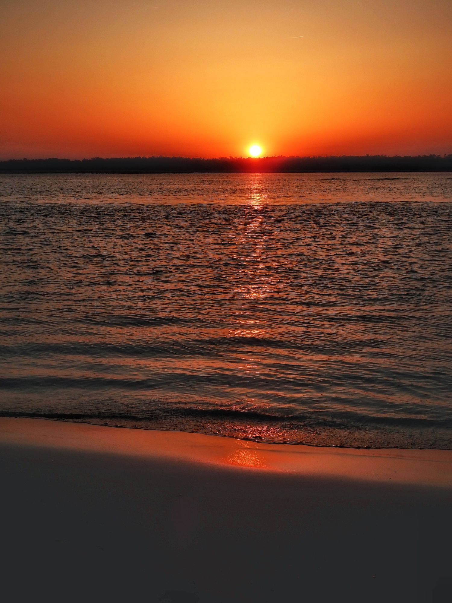 Golden sun setting over calm ocean waters with rippling reflections on the surface.