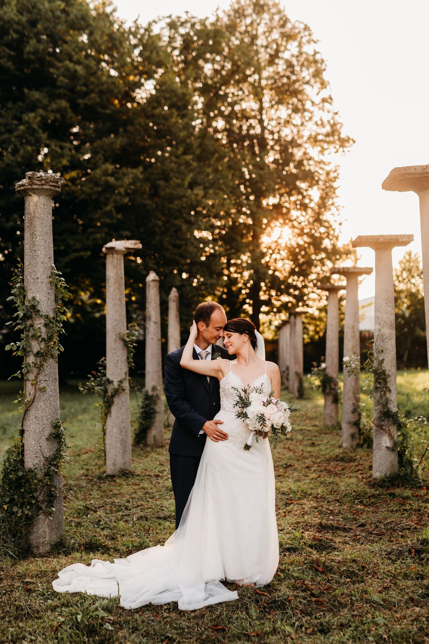 A romantic wedding portrait amidst ancient stone columns at golden hour.