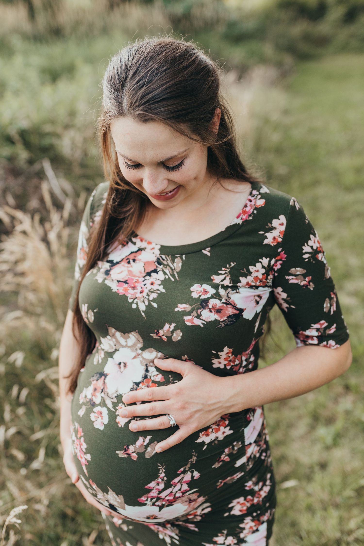 Young woman stands looking down at her pregnant belly at her maternity portrait near me