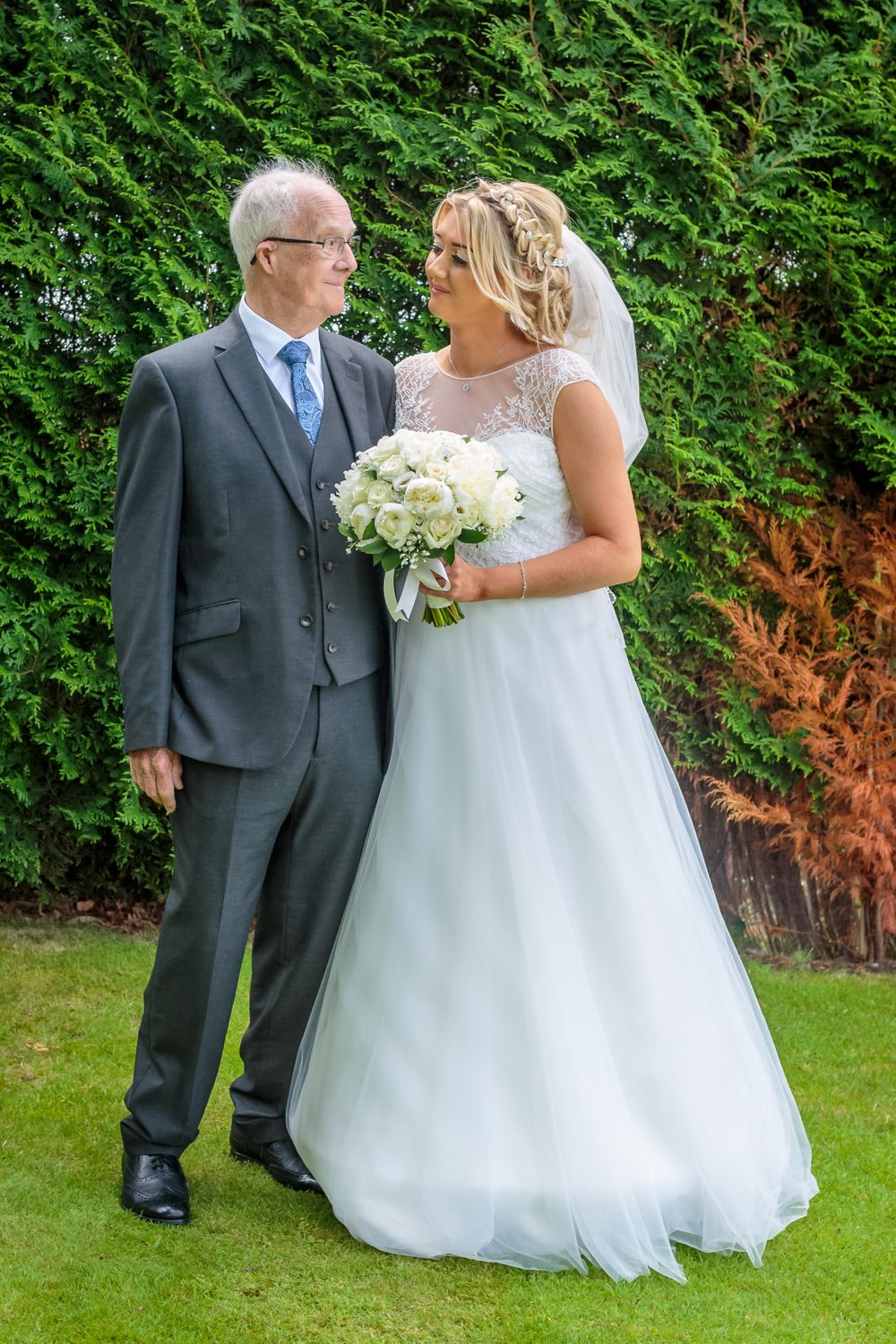 bride and her grandfather stand smiling at each other in the gardens at west tower