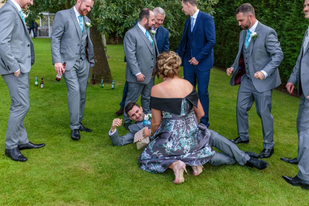 best man lying on the floor surrounded by the groomsmen with a lady kneeling over him