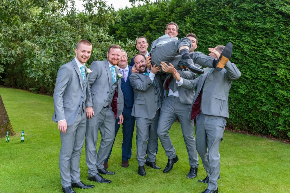 groomsmen lift the groom in the air in the garden at west tower wedding venue