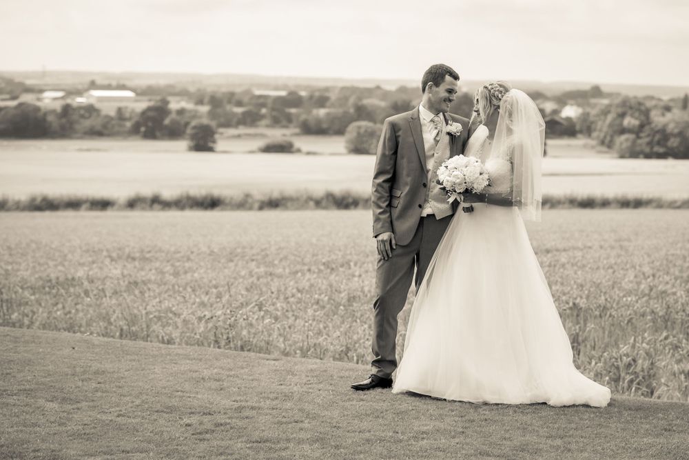 bride and groom smiling looking at each other in the gardens at west tower countryside in the background