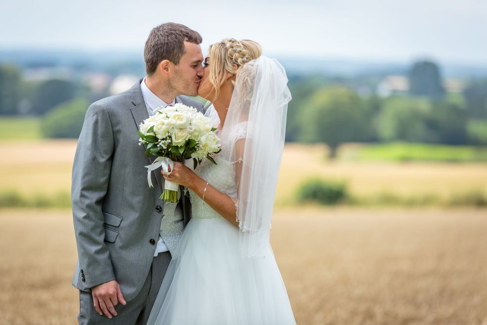 bride holding her bouquet kisses the groom with the countryside as a backdrop