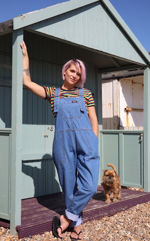 Model wearing fashion company, Run & Fly, dungarees outside a beach hut in Shoreham with a small brown dog.