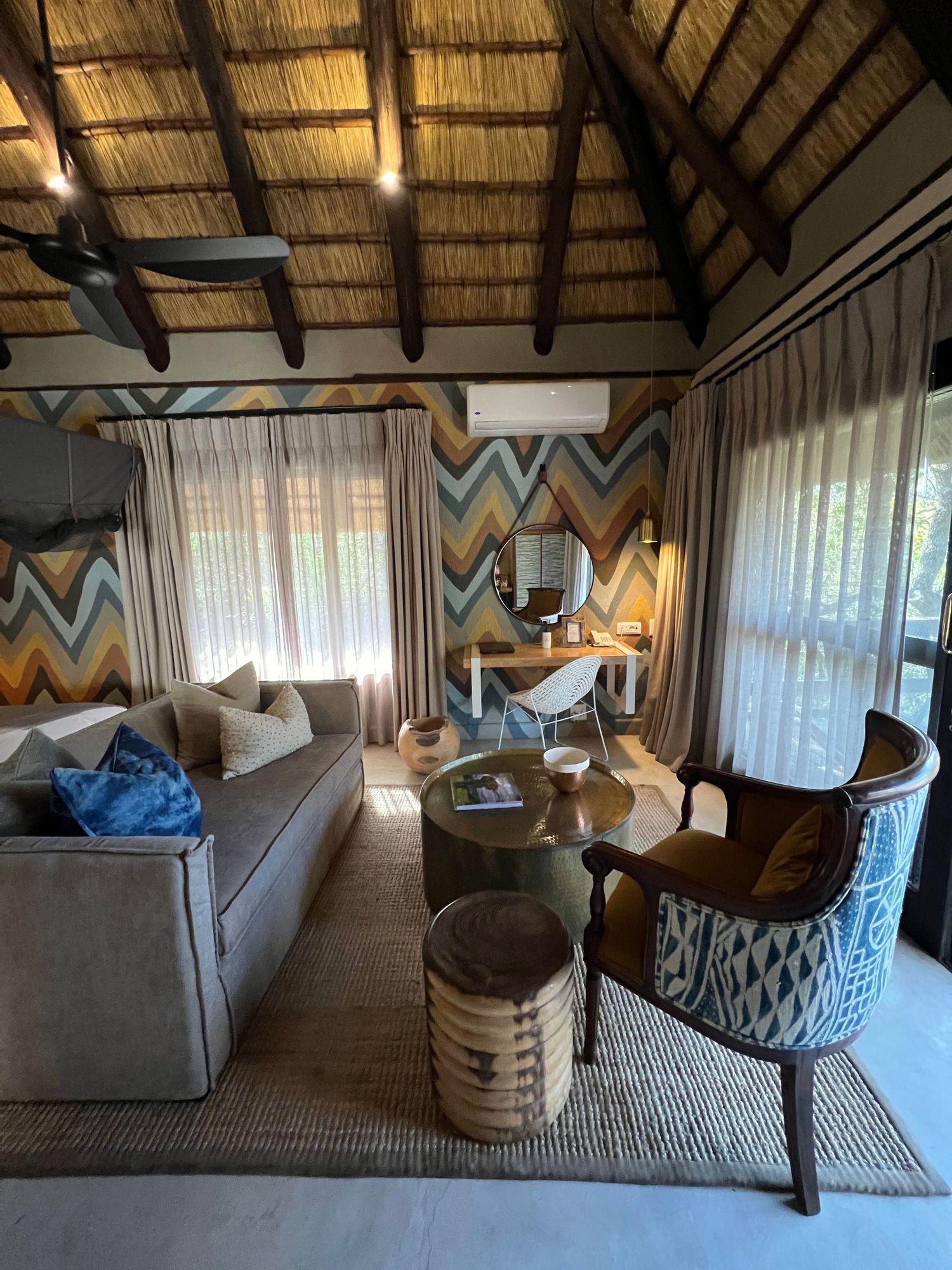 Safari lodge living room with chevron wall pattern, comfortable seating, and thatched ceiling design.