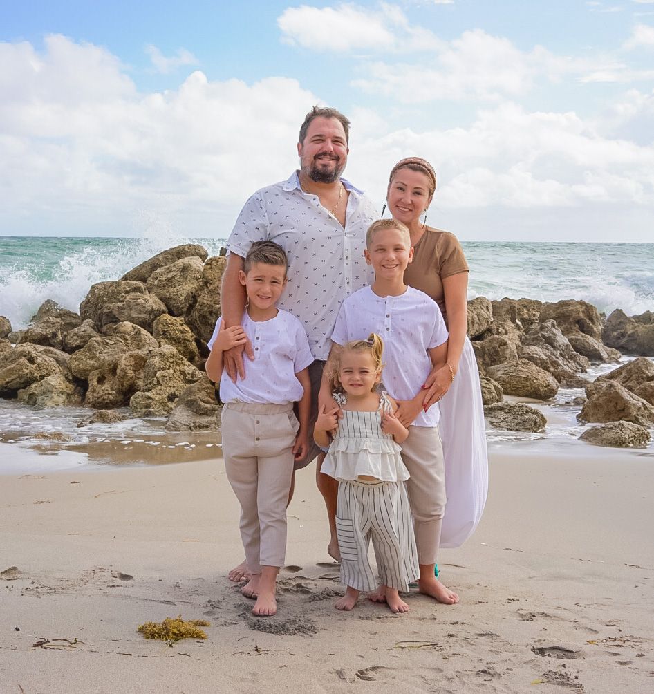 Happy family of five posing together on a rocky beach with ocean waves behind them.