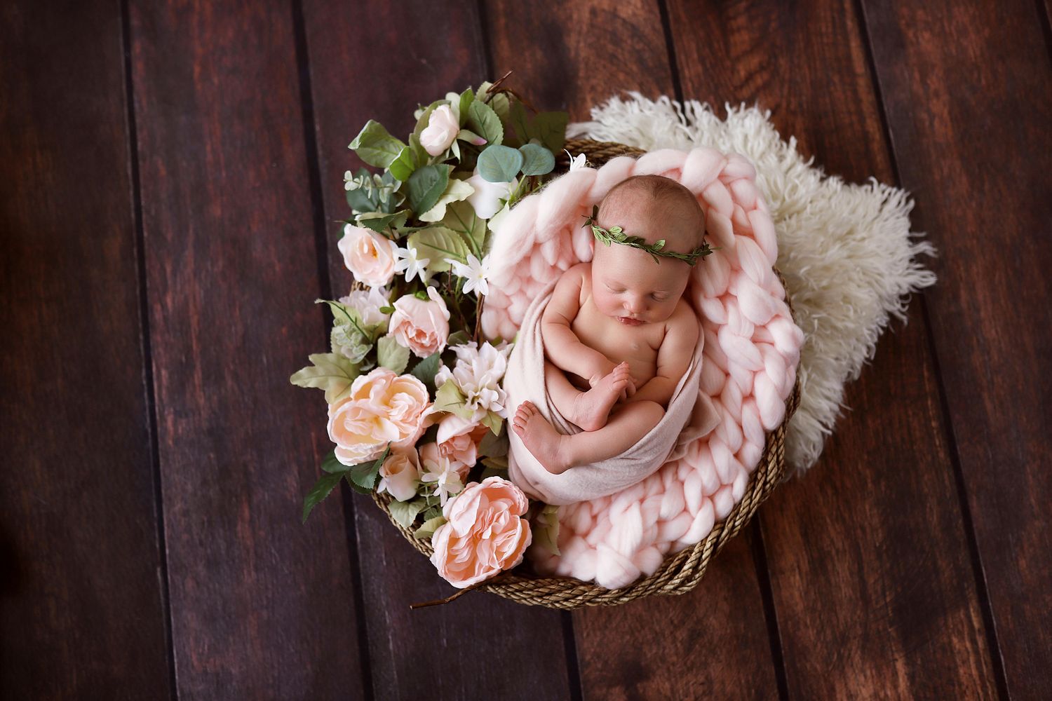 Dreamy newborn photography setup with pink wrap and roses in wooden basket.