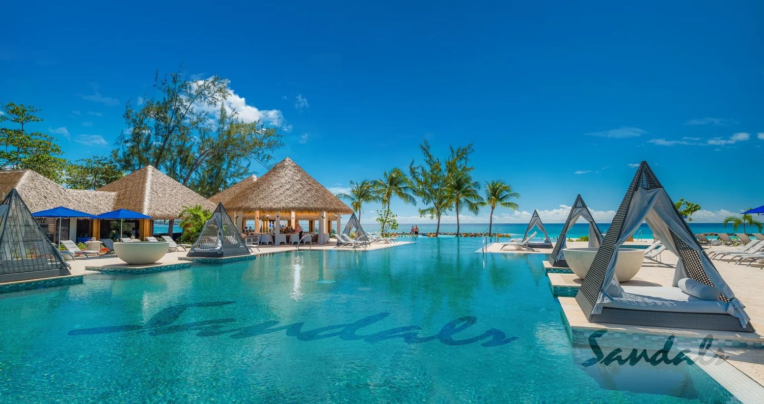 Tropical resort featuring thatched-roof cabanas and triangular daybeds surrounding a beachfront infinity pool.
