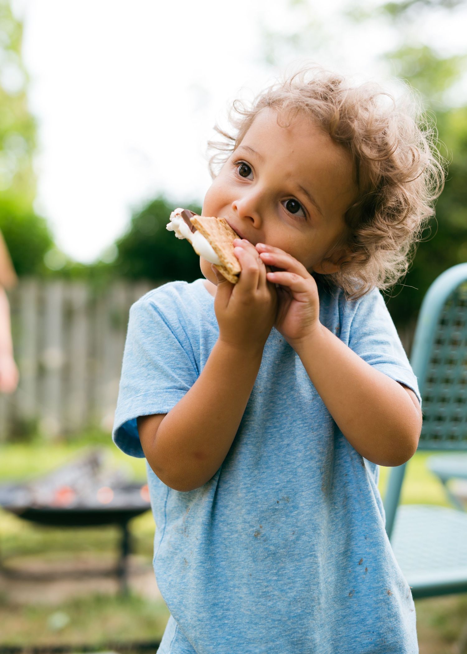 Young child in blue shirt eating food outdoors.