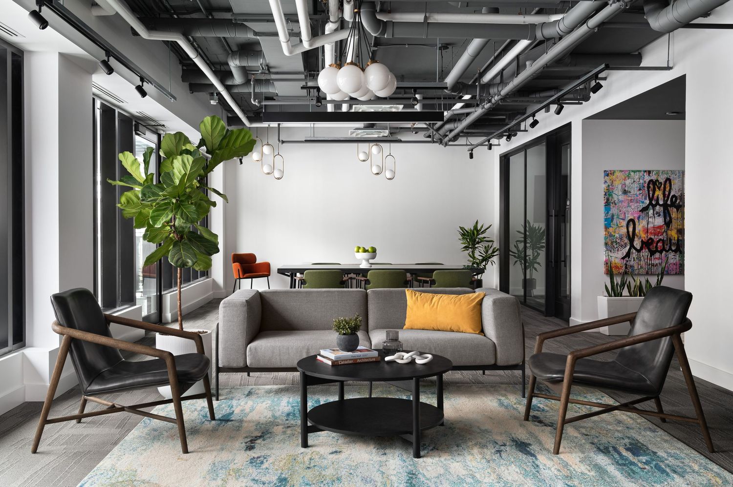 Modern industrial office lounge with grey furniture, plants, and exposed ceiling elements.
