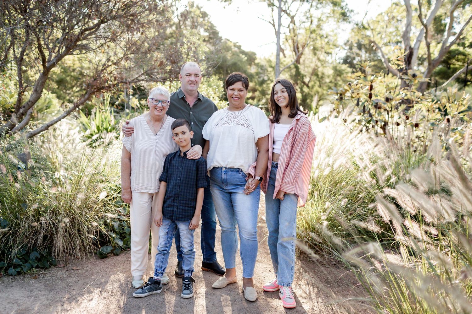 A group poses together on a nature trail surrounded by tall grass and trees.