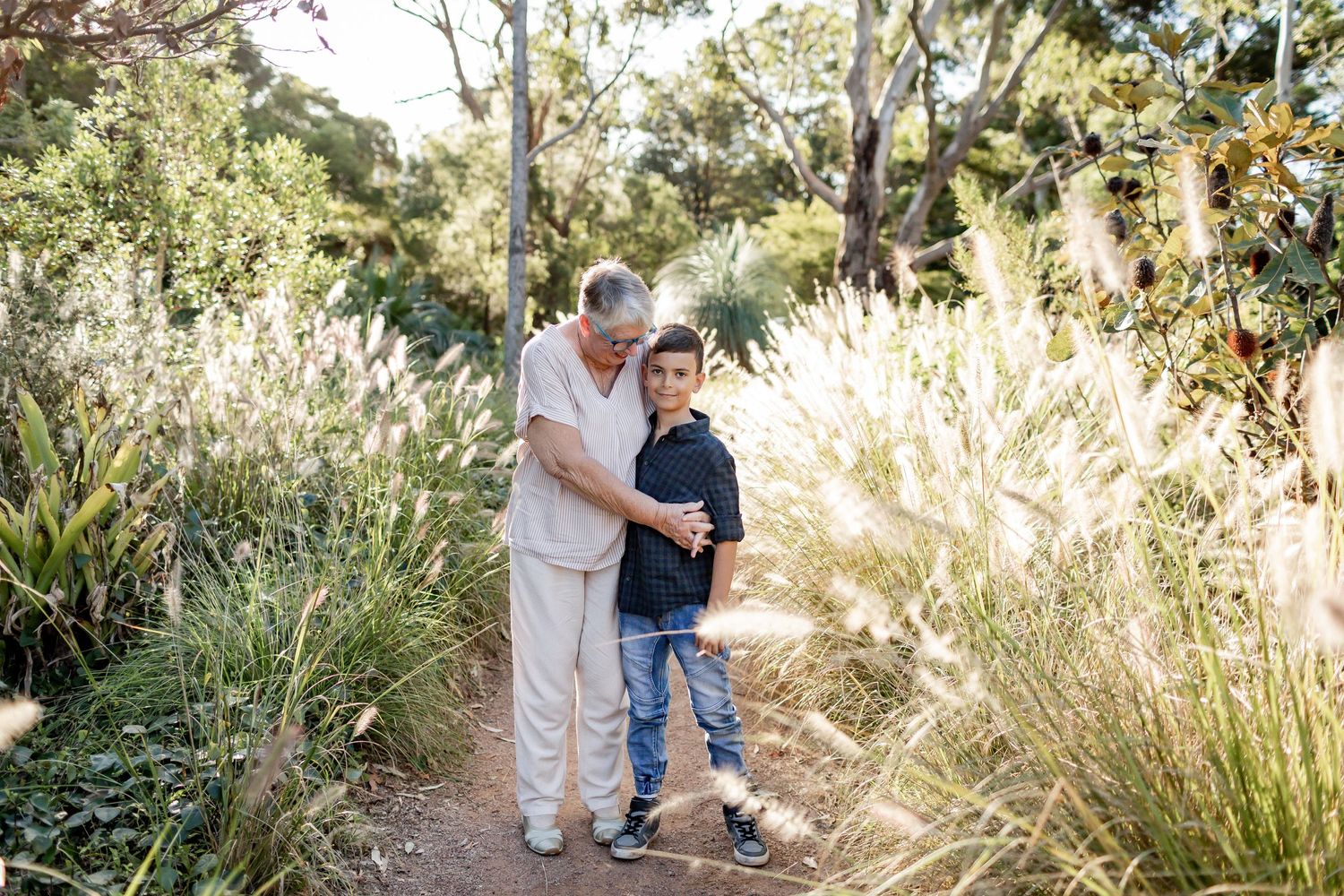 Two people walking together on a sunlit trail with pampas grass swaying in the background.
