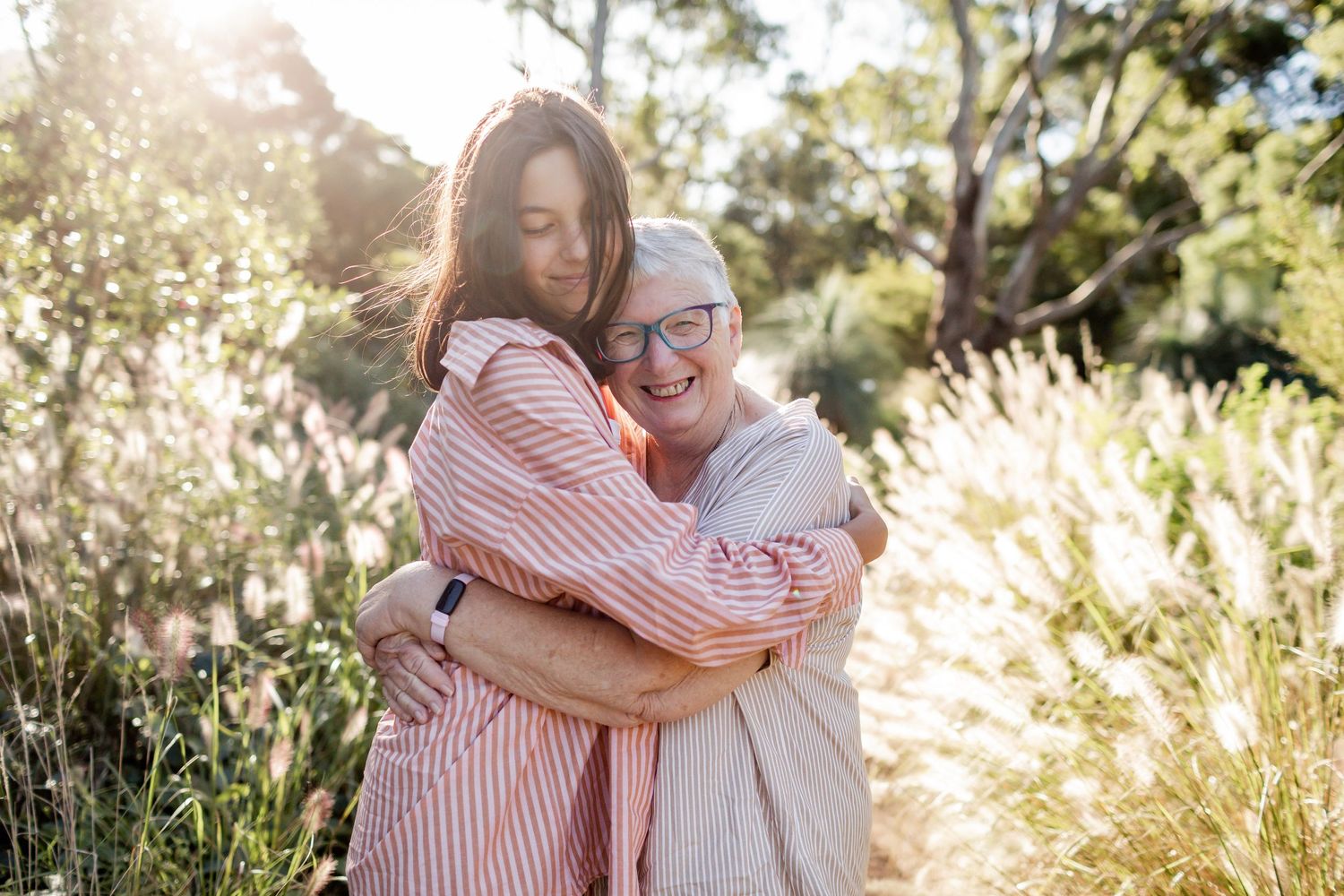 Two people share a warm embrace in golden sunlight on a nature trail.