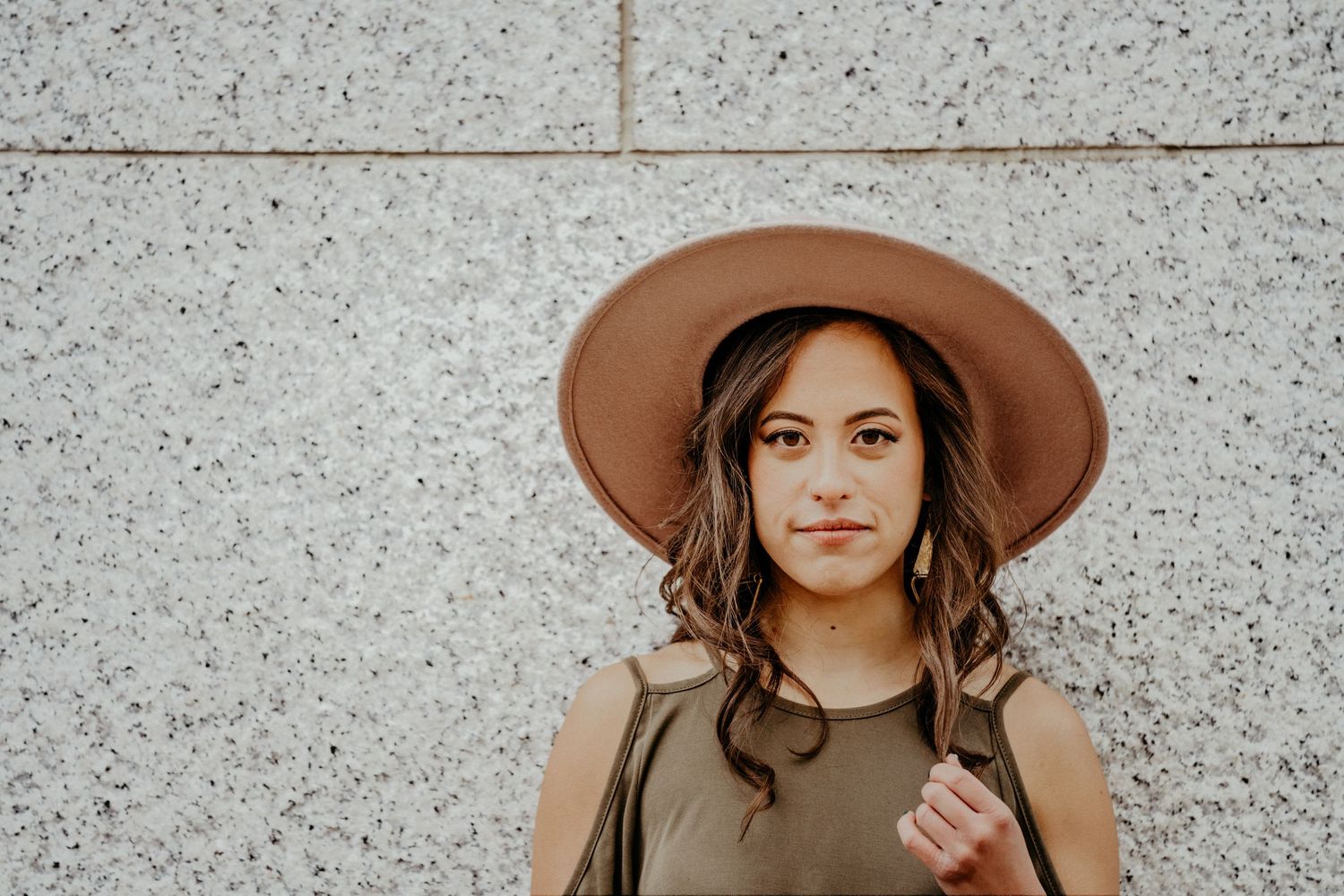 Woman in brown wide-brimmed hat standing against textured concrete wall.