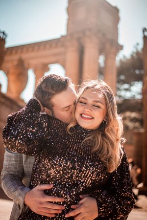 A couple shares an intimate moment in front of an ornate architectural structure during golden hour.