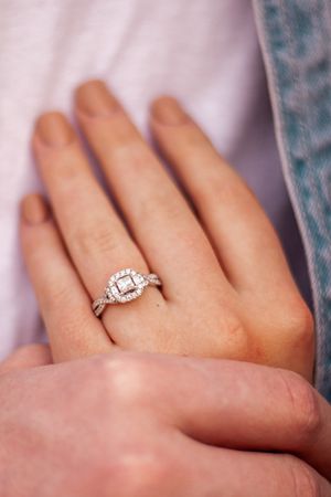 Close-up of a diamond engagement ring on a hand against a soft fabric background.