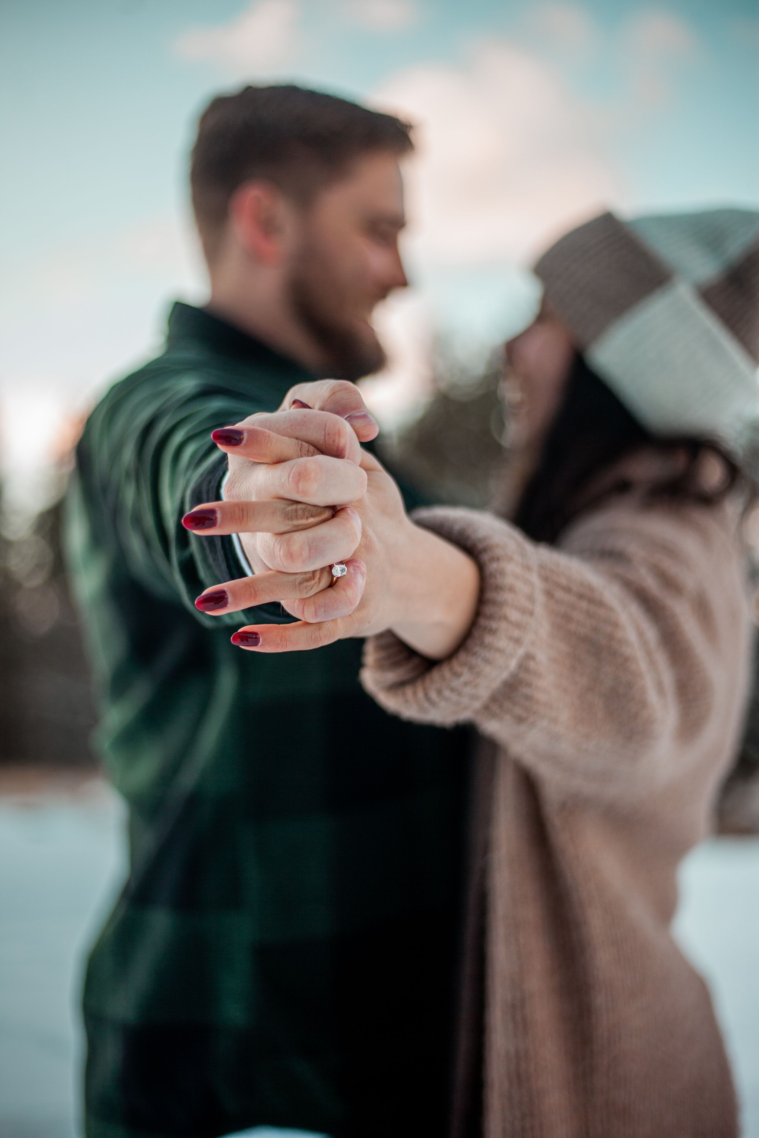 Intimate moment of two people holding hands while dancing in winter attire.