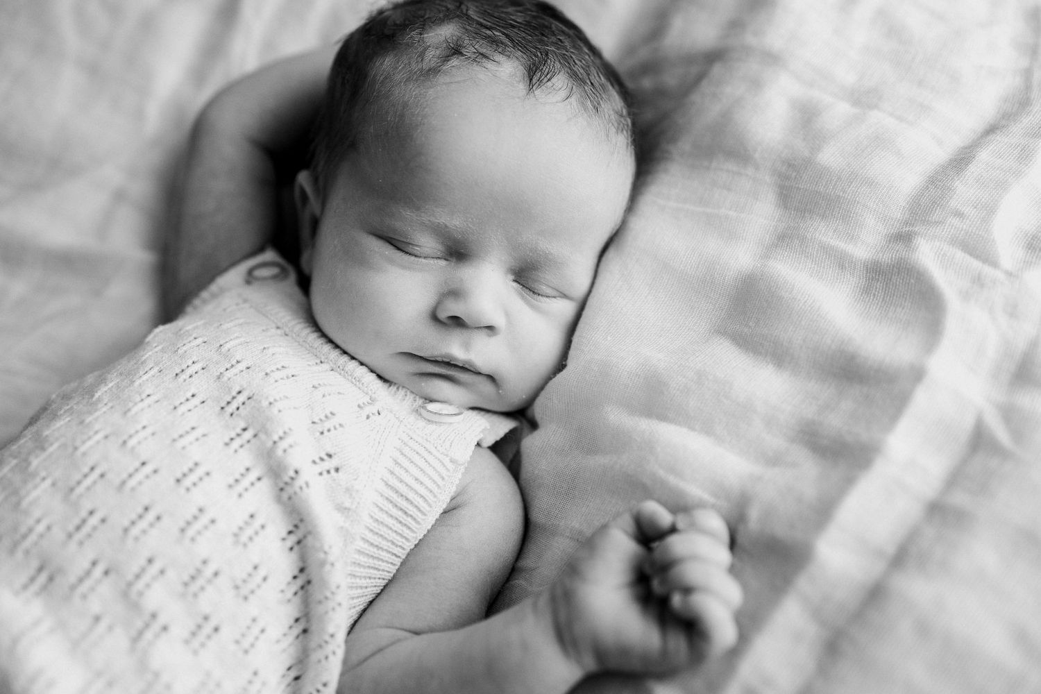 A sleeping newborn baby in black and white wearing a knitted sweater.