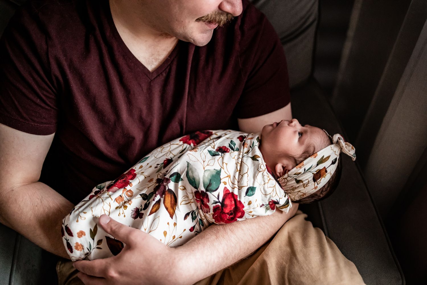 A baby swaddled in a floral print blanket being cradled in someone's arms.