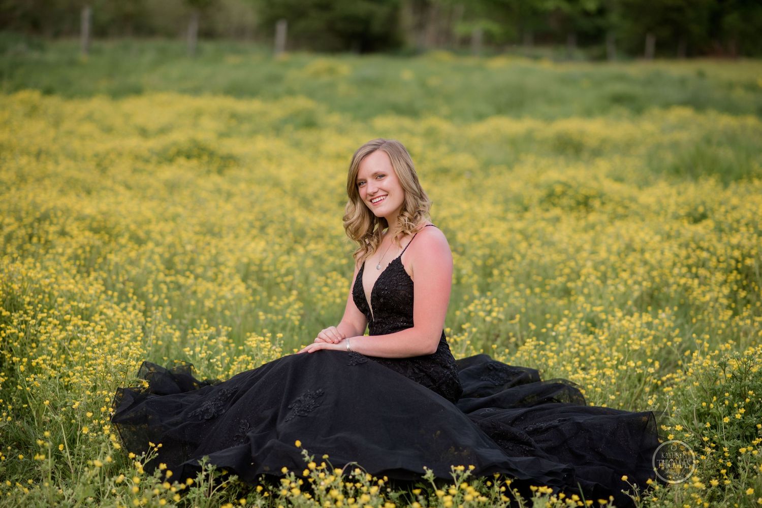 A figure in a flowing black gown sits gracefully among yellow wildflowers in a spring meadow.