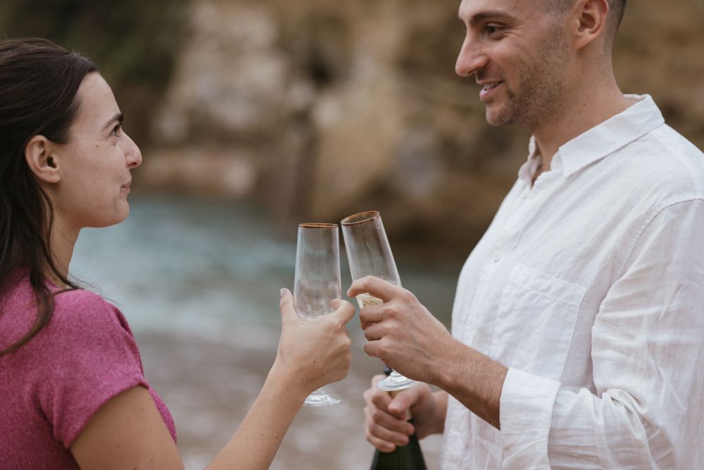 Close-up engagement toast on the shoreline, highlighting romantic coastal atmosphere.