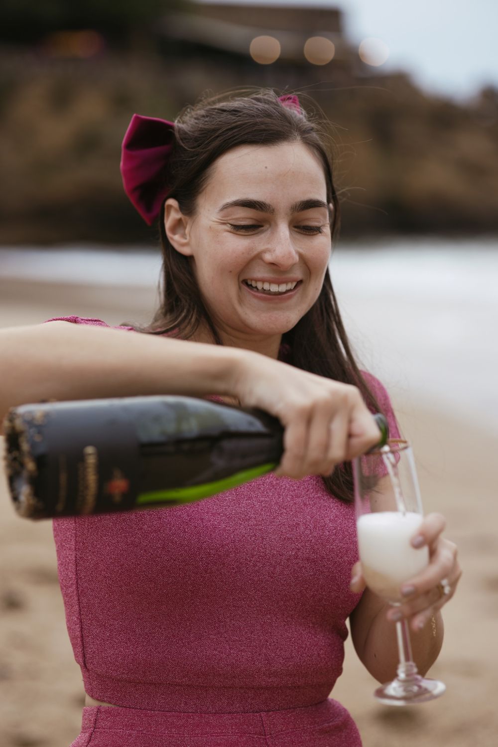 Woman pouring champagne on the beach during an elegant, relaxed engagement session.
