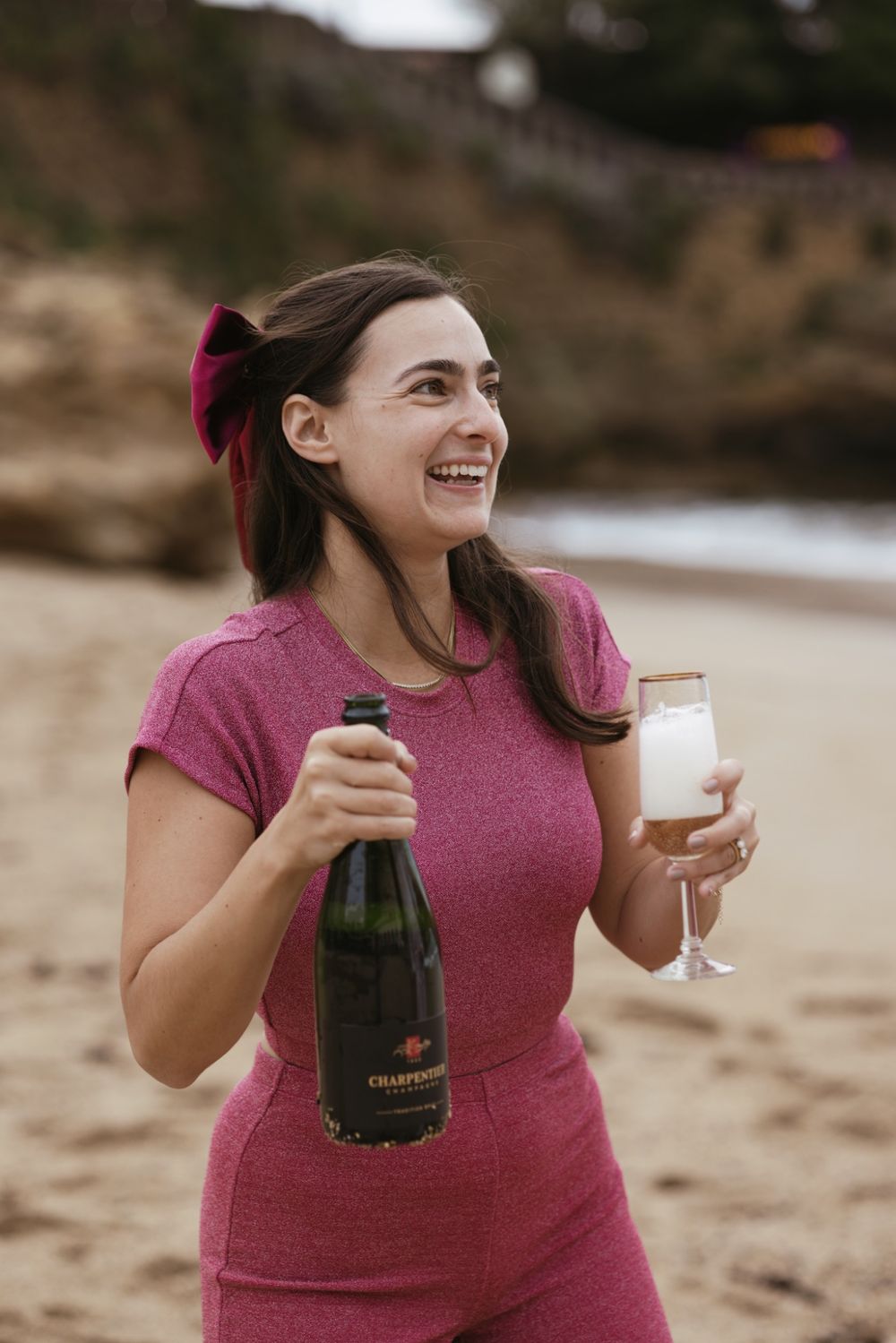 Portrait of a woman smiling with champagne during a seaside engagement session.