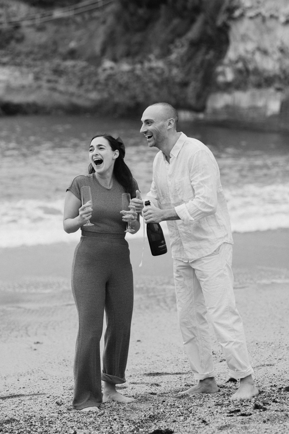 Candid engagement moment of a couple laughing together on the beach during a coastal photoshoot.