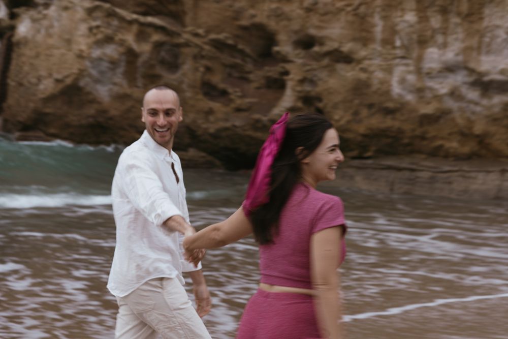 Couple walking hand-in-hand along the shoreline during a romantic engagement shoot.
