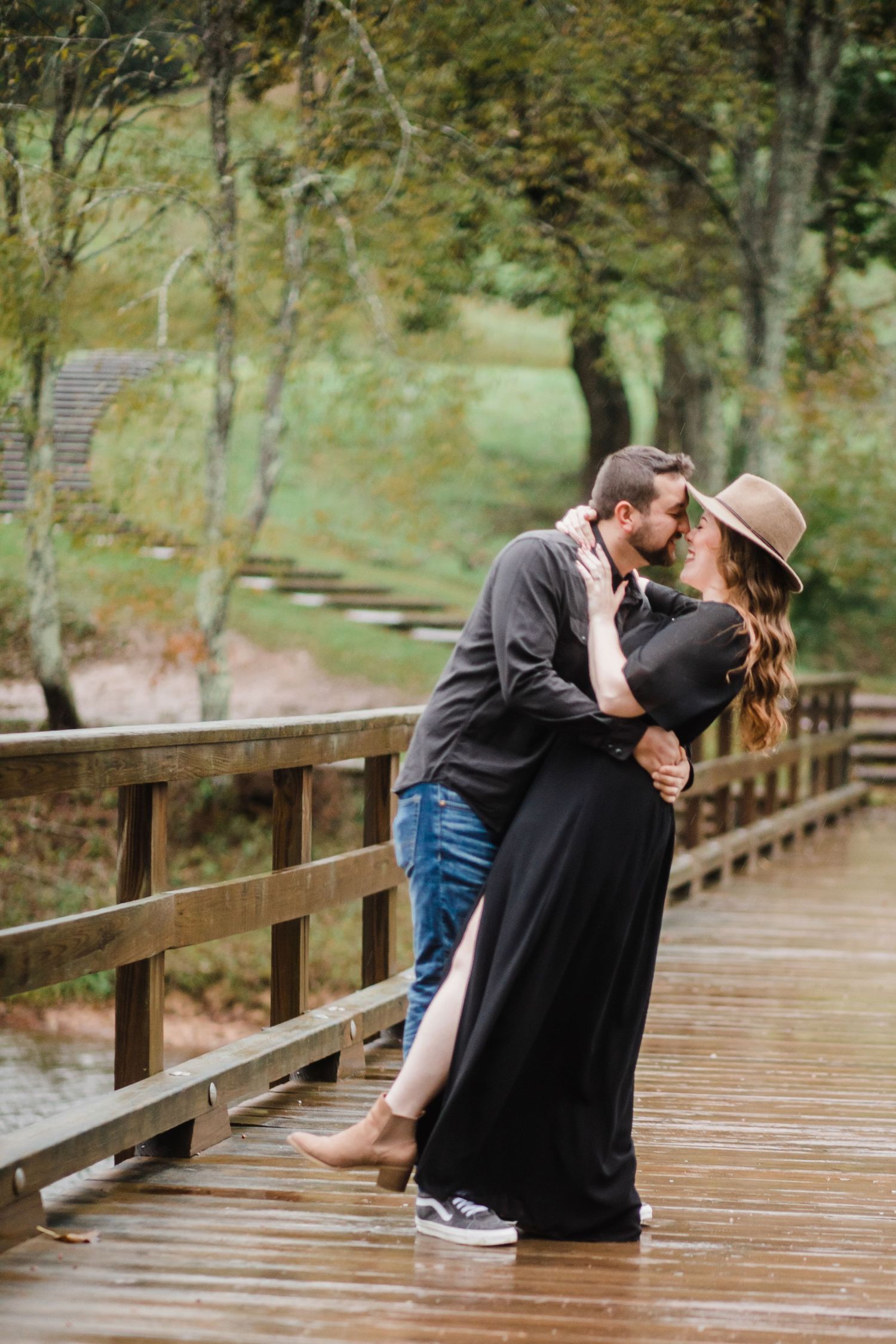 A couple shares a romantic kiss on a wooden boardwalk surrounded by autumn trees.