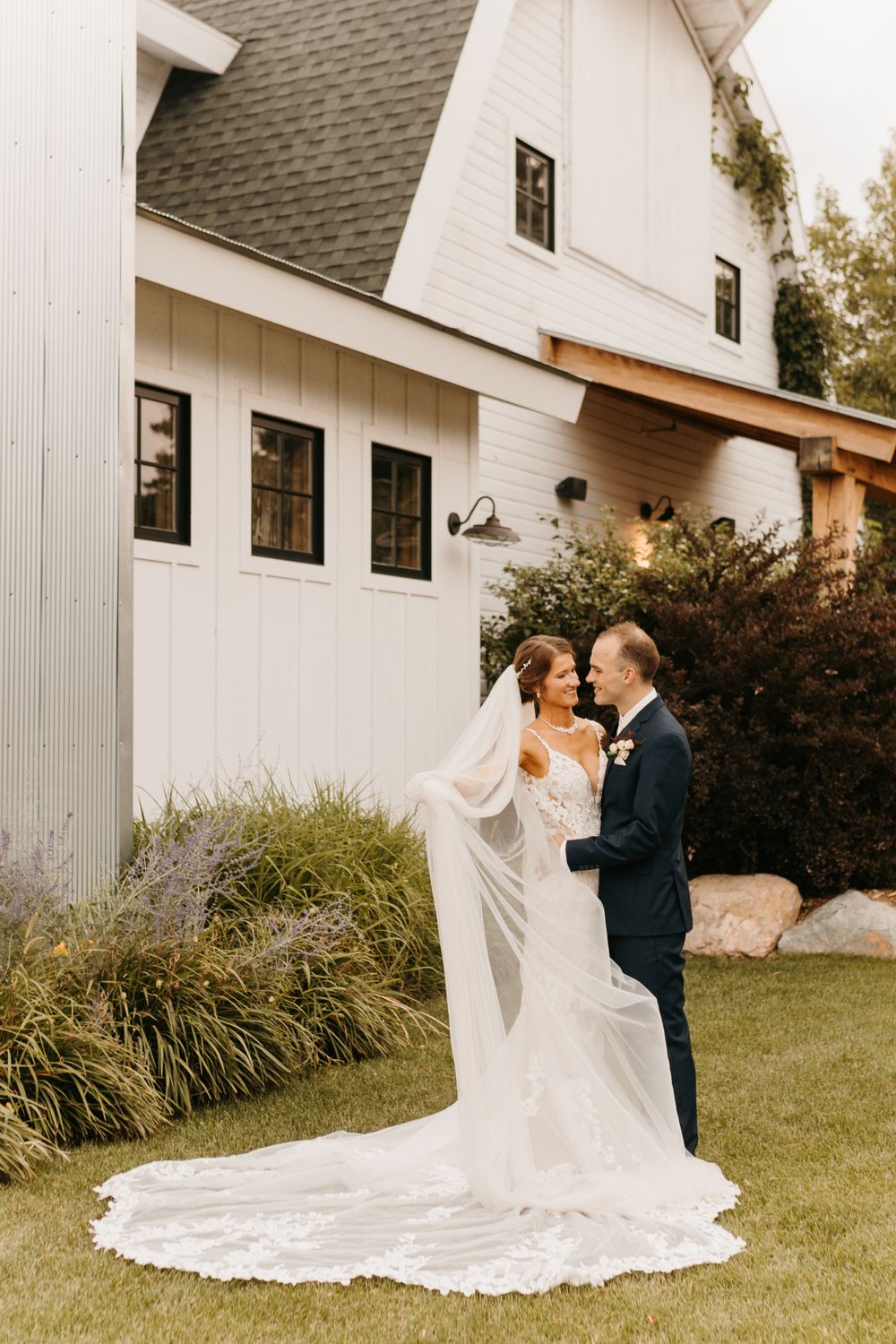 Bride and groom share romantic moment in front of white barn wedding venue at dusk.