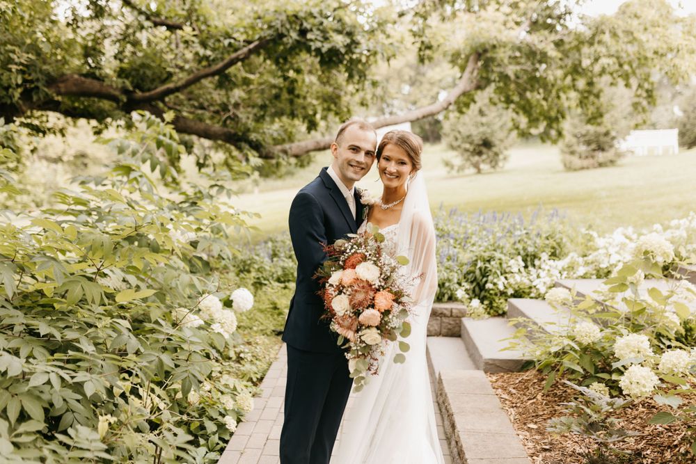 Happy bride and groom embracing outdoors surrounded by white hydrangeas and greenery.