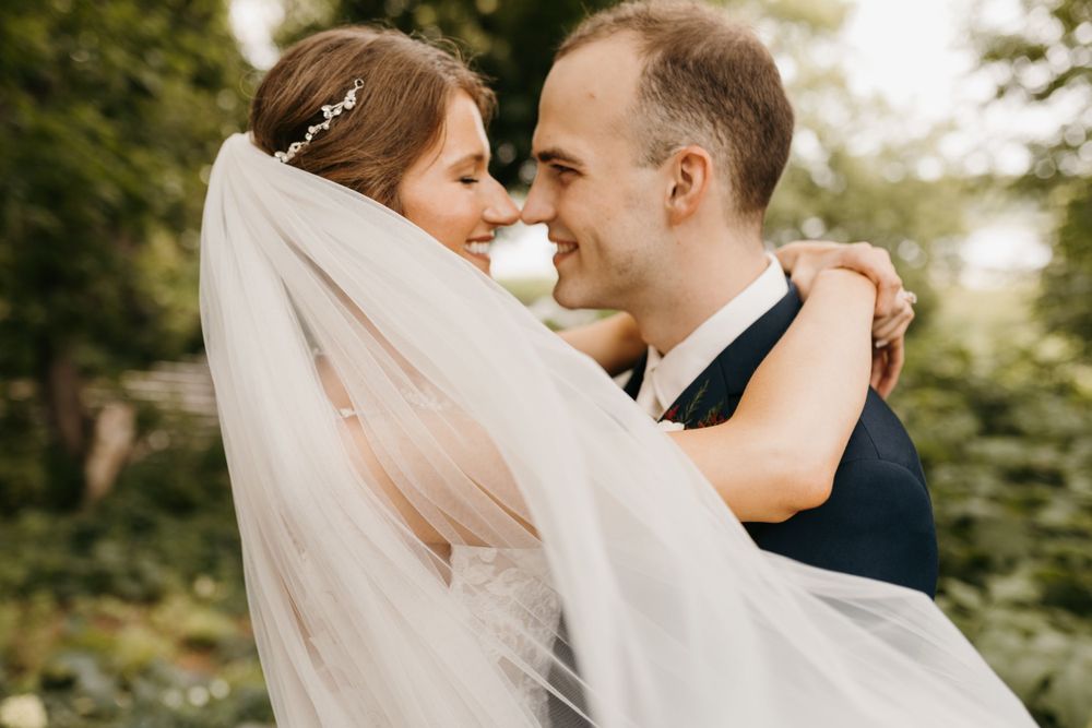 Bride and groom sharing an intimate moment, bride's veil draped around them both as they smile at each other.
