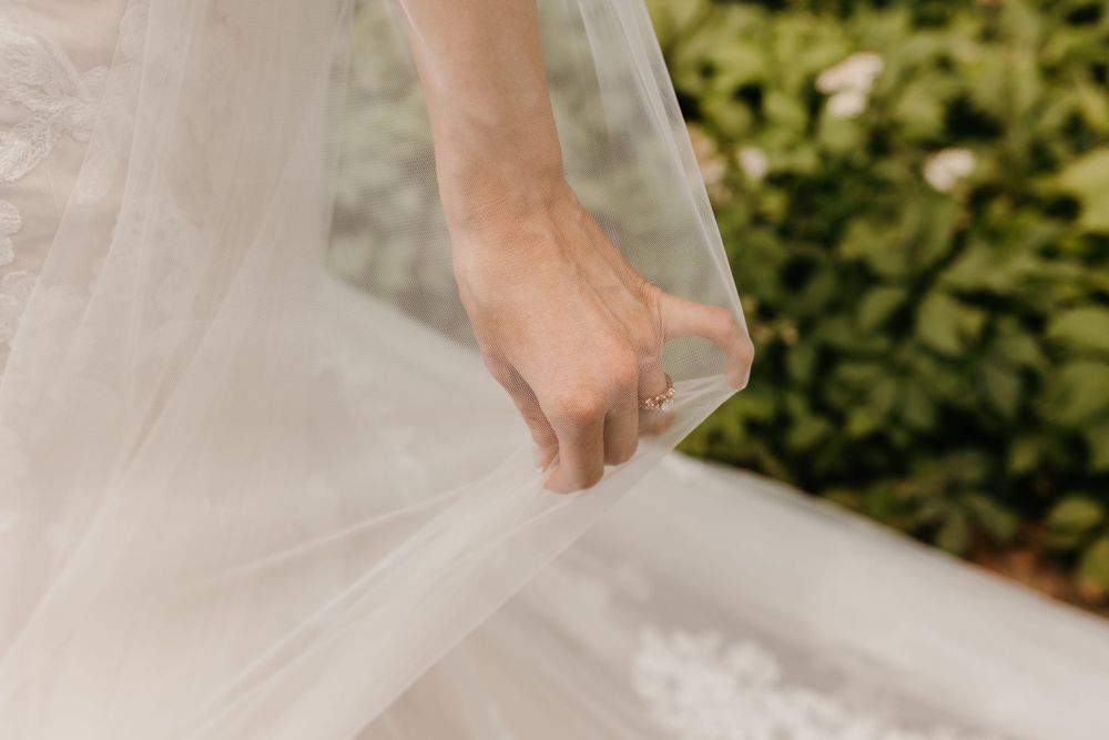 Close-up of bride holding delicate tulle veil with diamond engagement ring visible.