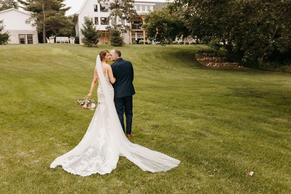 Bride and groom walk hand in hand on manicured lawn with elegant lace bridal train.