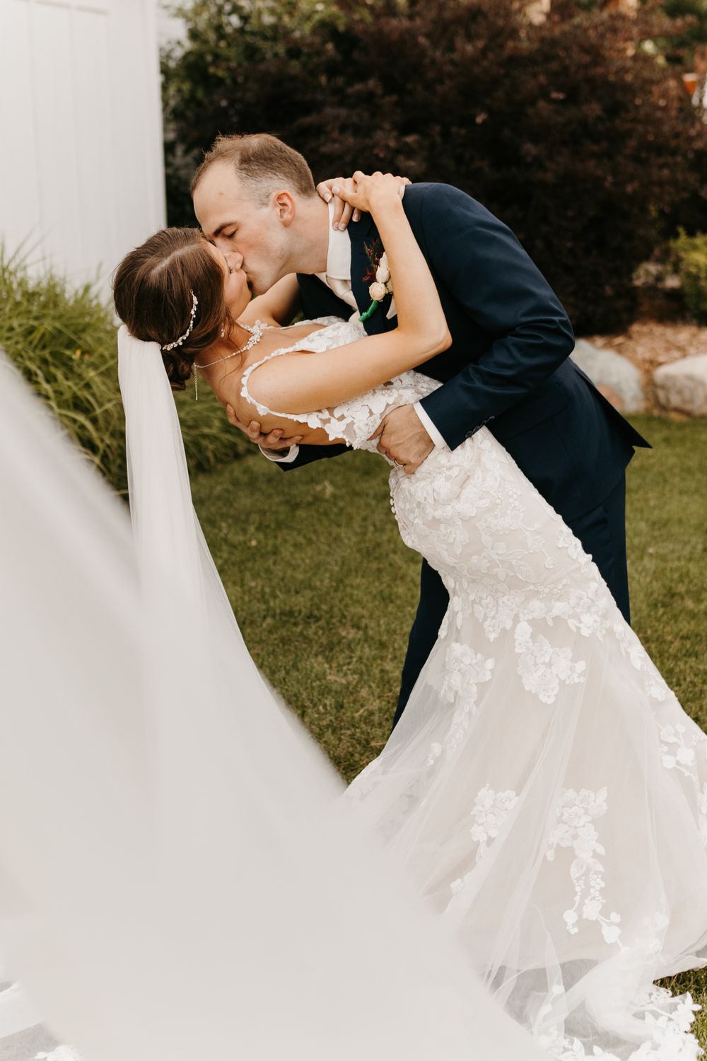 Groom dips bride for passionate kiss in lace mermaid gown with flowing cathedral veil.
