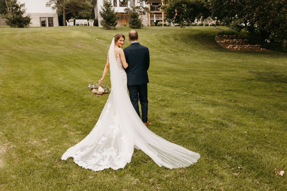 Aerial view of bride and groom walking on green lawn with lace cathedral train.