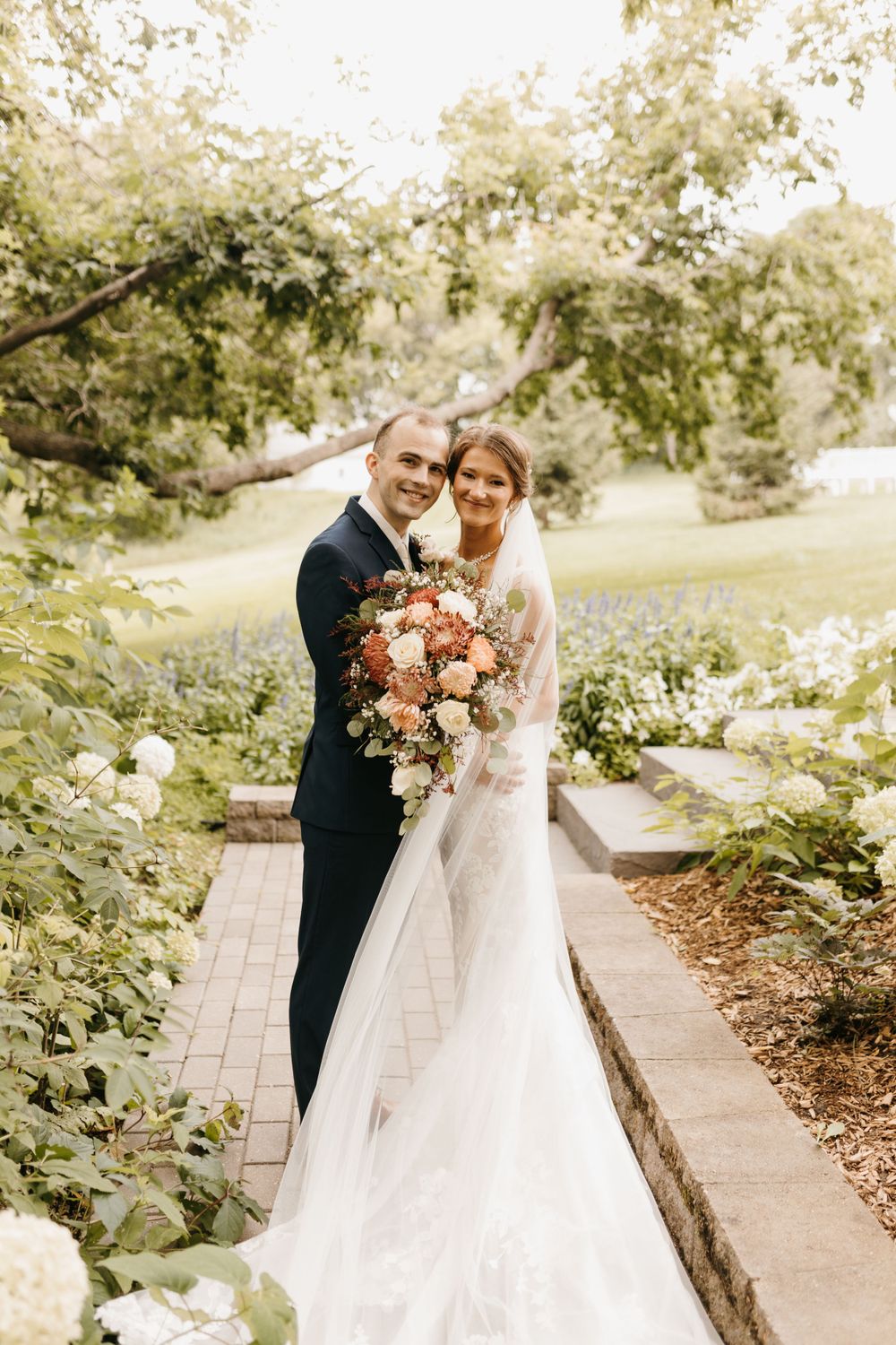 Bride and groom posing with colorful cascading bouquet in lush garden setting.
