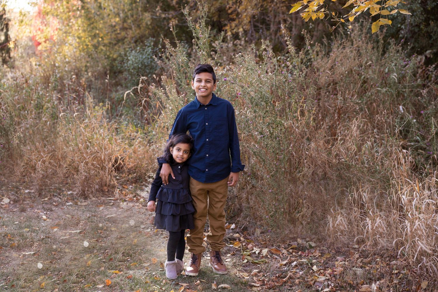 Two people standing together in tall autumn grasses during a golden hour photoshoot.