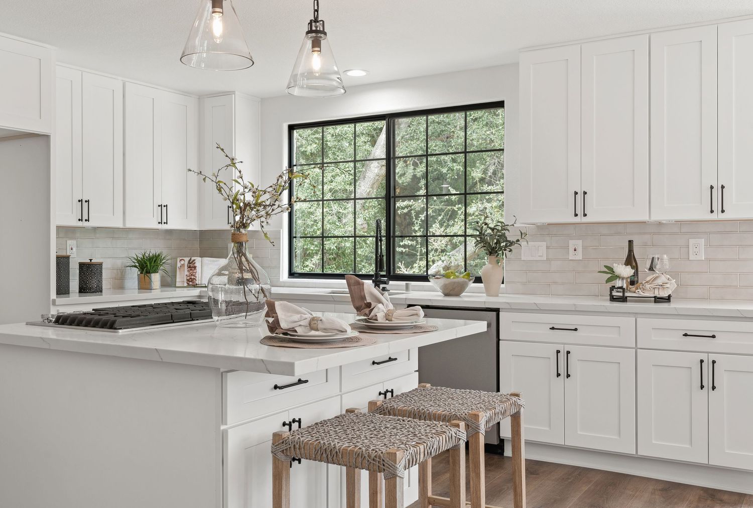 Bright white kitchen with shaker cabinets, window view, and woven counter stools at peninsula.