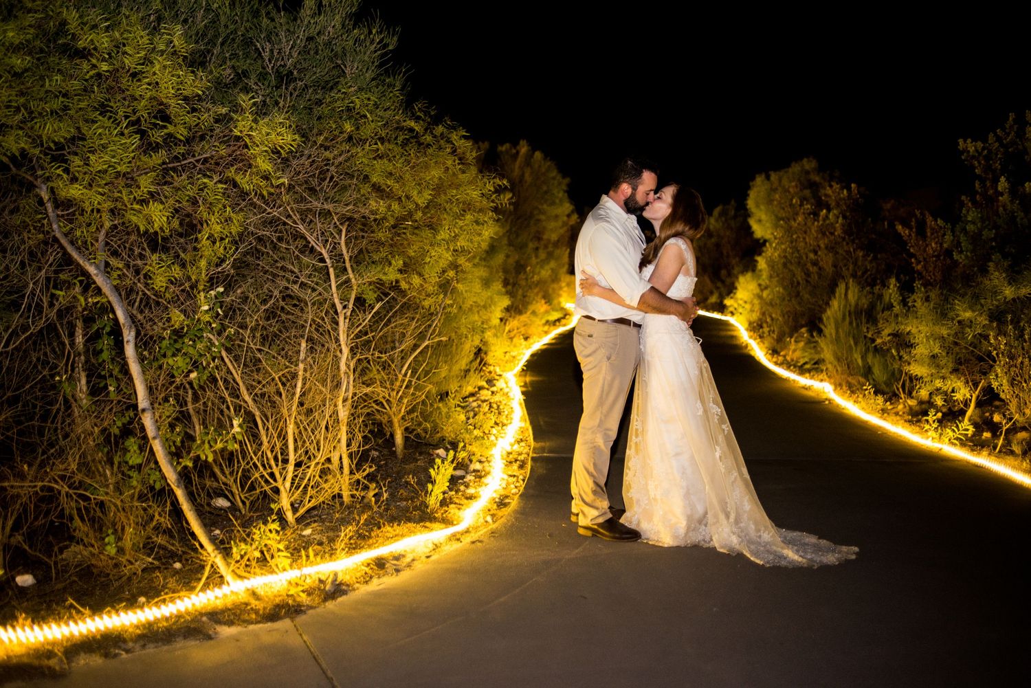 A couple poses on a path illuminated by string lights creating a magical nighttime wedding scene.